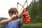Young guy takes aim, preparing to make shot from slingshot. portrait boy is going to shoot on background of nature. Child outdoor