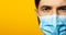 Young guy wearing medical respiratory face mask against coronavirus. Panoramic portrait on yellow background with copy space.