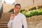 Young guy in a white shirt stands and smiles near the stairs and flowers at sunset