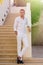 Young guy in a white shirt stands and smiles near the stairs and flowers at sunset