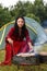 A young gypsy woman grills meat on the grill near the tent in the smoke of the fire. Horizontal photo