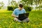 Young gyu freelincer at work on a laptop on a green grass and trees background