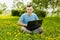 Young gyu freelincer at work on a laptop on a green grass and trees background