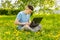 Young gyu freelincer at work on a laptop on a green grass and trees background