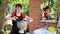 Young hairdresser makes haircut to a woman in front of mirror in the yard outdoors on summer day