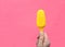 Young hand holding yellow cake popsicle over pink background