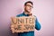 Young handsome activist man asking for union holding banner with united stand message serious face thinking about question, very