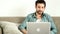 Young handsome adult man sitting on couch in living room and having video chat