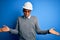 Young handsome african american engineer man with dreadlocks wearing safety helmet clueless and confused expression with arms and