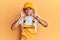 Young handsome african american man wearing handyman uniform over yellow background trying to hear both hands on ear gesture,