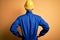 Young handsome african american worker man wearing blue uniform and security helmet standing backwards looking away with arms on