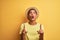 Young handsome arab man wearing t-shirt and summer hat over isolated yelllow background amazed and surprised looking up and