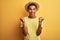 Young handsome arab man wearing t-shirt and summer hat over isolated yelllow background celebrating surprised and amazed for