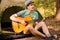 Young handsome attractive bearded model man in hat playing guitar in forest.