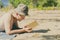 Young handsome attractive man in panama lying on sandy heaven beach and reading a book on a summer day