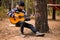 Young handsome attractive man in sweater playing guitar in forest sitting on swing. Casual man, life style