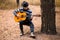 Young handsome attractive man in sweater playing guitar in forest sitting on swing. Casual man, life style