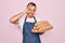 Young handsome baker man with blue eyes wearing apron holding tray with wholmeal bread with happy face smiling doing ok sign with