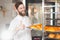 A young handsome baker shows his thumb up with a sheet of fresh croissants in his hands against the backdrop of an oven.