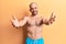 Young handsome bald man wearing swimwear shirtless looking at the camera smiling with open arms for hug