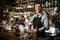 Young handsome bartender holds in his hands steel shaker and empty glass