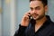 Young handsome bearded Indian businessman talking on the phone in the city