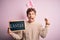 Young handsome blonde man wearing easter rabbit ears and holding blackboard with holiday word screaming proud and celebrating