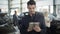 Young handsome brown-eyed Caucasian man standing in car dealership with tablet, looking at camera and smiling. Confident