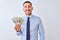 Young handsome business man holding a bunch of bank notes dollars over isolated background with a happy face standing and smiling