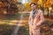 Young handsome businessman walking in autumn forest at sunset. Stylish guy wearing classic clothes and accessories