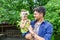 Young handsome caucasian male with eyeglasses carrying his little lovely baby girl in yellowish clothes in garden