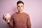 Young handsome caucasian man holding piggy bank for savings over pink background with a confident expression on smart face