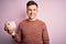 Young handsome caucasian man holding piggy bank for savings over pink background with a happy face standing and smiling with a