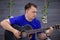 Young handsome caucasian man playing guitar in romantic ambience. Musician practising, casual blue wear, gray wall background