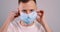 Young handsome caucasian man puts on face medical mask. Close-up portrait on gray background.