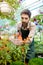 Young handsome cheerful gardener smiling, watering, taking care of flowers.