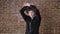 Young handsome cheerful man with curly hair dancing and looking at camera, brick wall background