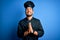 Young handsome chef man with beard wearing cooker uniform and hat over blue background begging and praying with hands together