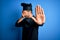 Young handsome chef man with beard wearing cooker uniform and hat over blue background covering eyes with hands and doing stop