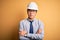 Young handsome chinese architect man wearing safety helmet and tie over yellow background skeptic and nervous, disapproving