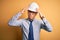 Young handsome chinese architect man wearing safety helmet and tie over yellow background suffering from headache desperate and