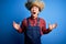 Young handsome chinese farmer man wearing apron and straw hat over blue background crazy and mad shouting and yelling with