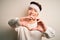 Young handsome chinese man injured for accident wearing bandage and strips on head smiling in love doing heart symbol shape with