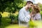 Young handsome couple dressed in vintage costume standing on embankment by river and under trees, kissing.