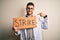 Young handsome doctor man protesting holding cardboard with strike message with surprise face pointing finger to himself