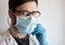 A young handsome doctor wearing glasses and a medical face mask puts on a stethoscope while preparing for a patients examination