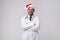 Young handsome doctor in white uniforme and Santa Claus hat standing in studio on white background loking at camera abd teeth