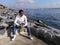 Young handsome european man sits on large granite boulders on the embankment of the Bosphorus in Istanbul Turkey. An adult