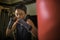 Young handsome and fierce 13 or 14 years old boy in wrist wraps doing fight workout punching heavy bag looking cool and badass at