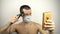 A young handsome guy in a protective mask cuts his own hair with an electric trimmer during a pandemic. A young guy in a